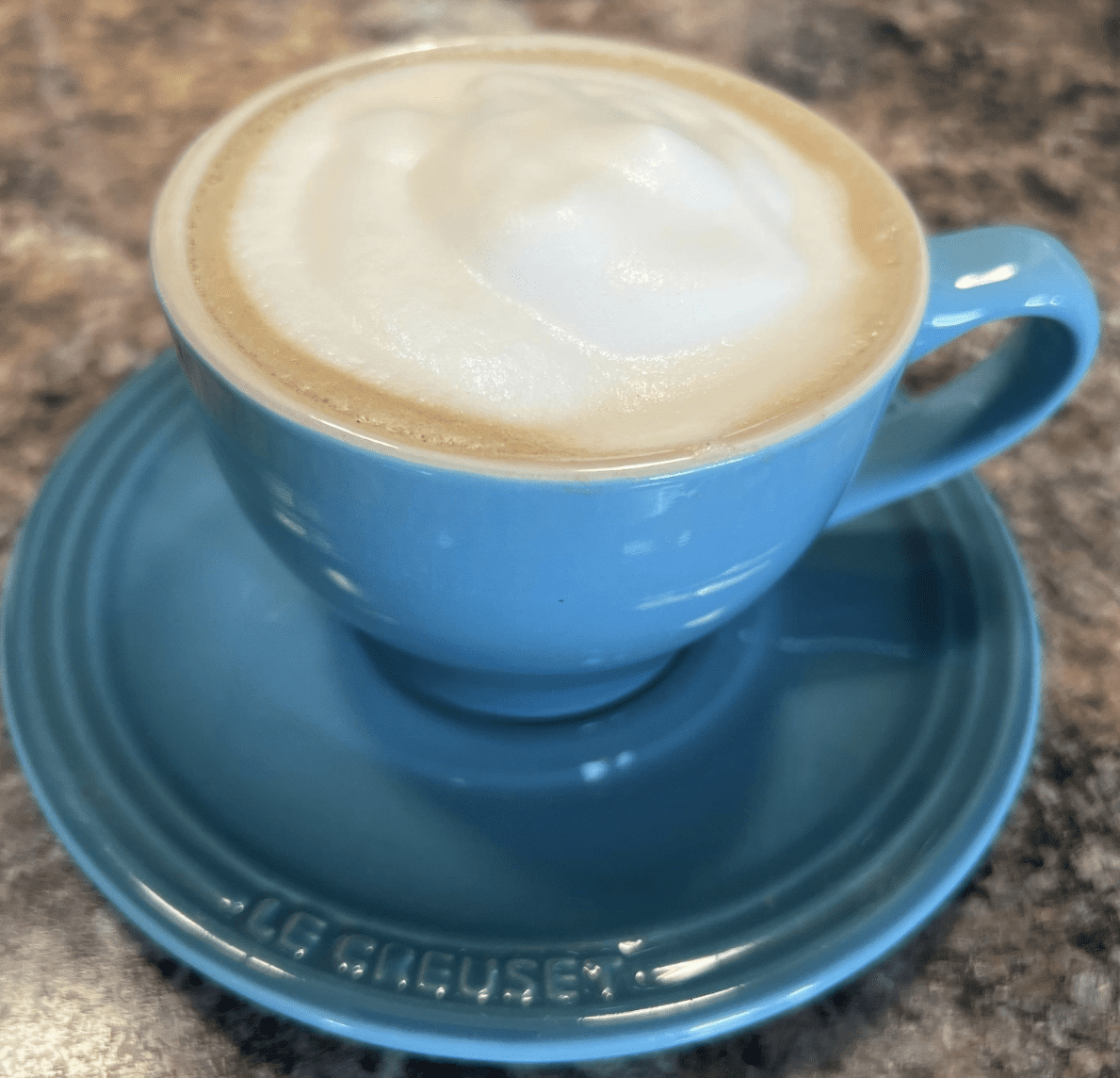 Blue cup with frothy cappuccino on saucer.