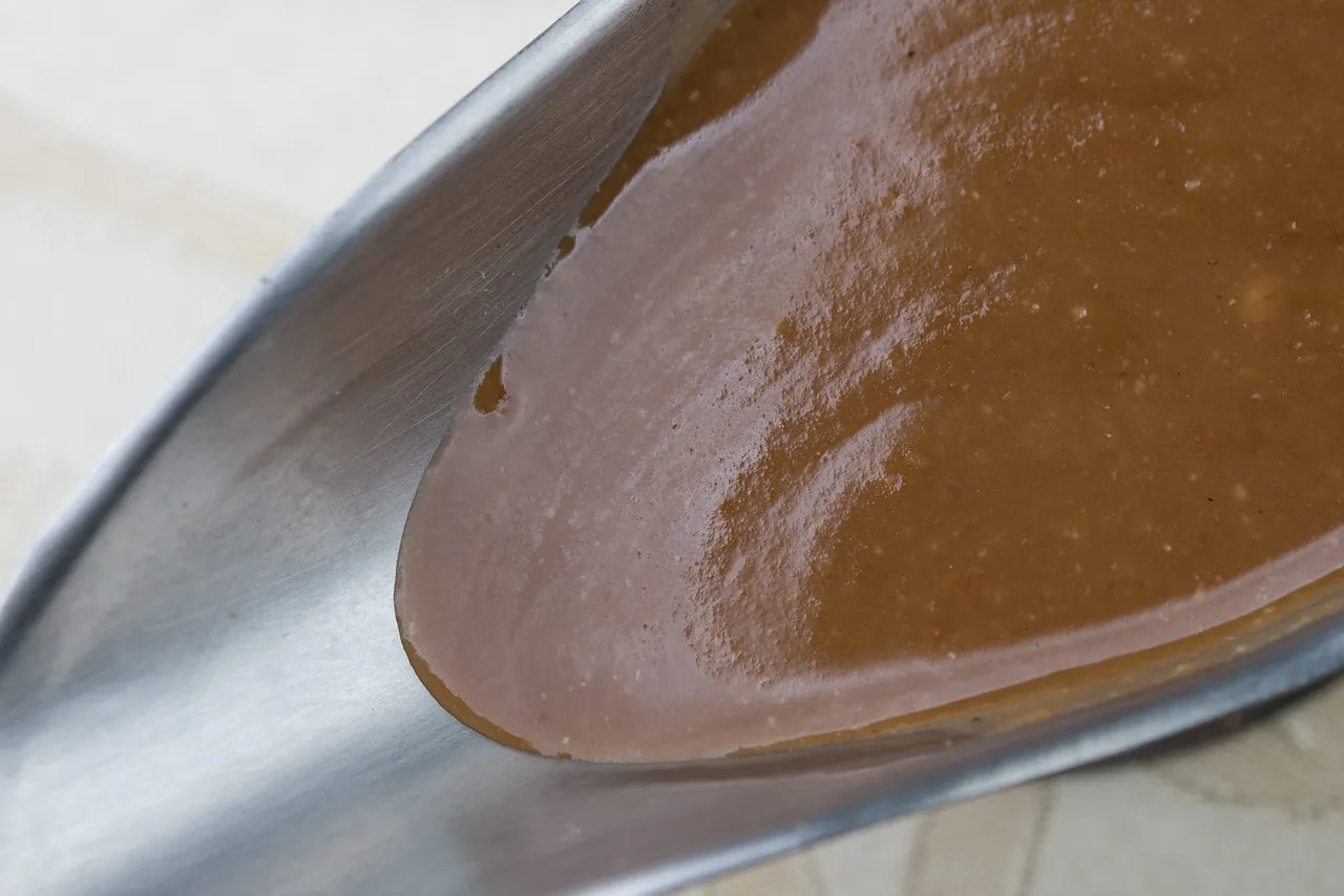Scoop of brown sauce on metal spoon.