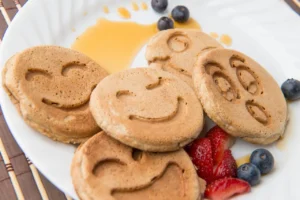 Smiley face pancakes with berries and syrup.